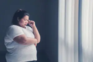 obese woman thinking something while standing near the window