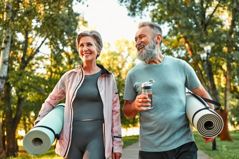 Happy sports couple going for a workout outdoors, holding exercise mats and water.